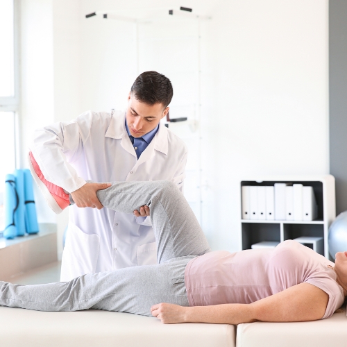Male therapist assisting female patient with physical therapy knee movements.